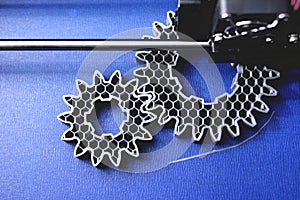 FDM 3D-printer manufacturing spur gears from silver-gray filament on blue print tape - top view