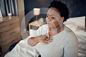 Fear, bedroom and black woman with an anxiety attack or pain in chest from stress. Scary, health and an African girl on
