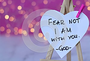 Fear not, I am with you, handwritten text verse on heart-shaped note with blurred bokeh background