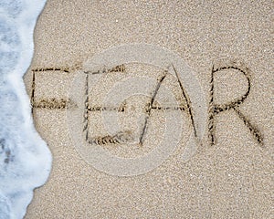 Fear word hand written with wave foam on sand beach