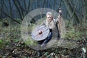 Viking woman warrior in forest with shield and sword in hand covered in blood.