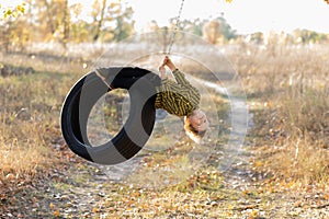 A fearless little boy swings on a wheel suspended from a tree