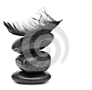 Feather balancing on stack of black stones