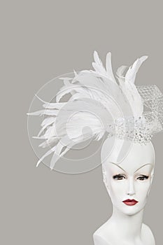 Feather fascinator on mannequin against gray background