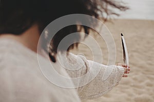 Feather in hand of beautiful woman with windy hair on background of sandy beach and sea, tranquil moment.  Free and wild. Stylish