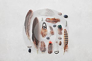 Feather pattern with pebble on gray stone background top view in flat lay style for boho theme.