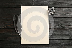 Feather pen, inkwell and blank parchment on wooden table, top view