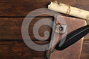 Feather pen, inkwell, old book and parchment scroll on wooden table, flat lay. Space for text