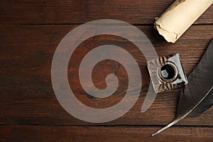 Feather pen, inkwell and parchment scroll on wooden table, flat lay. Space for text