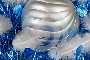 Feather and silvery Christmas ball on a blue tinsel