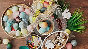 Feathers falling on colorful Easter eggs in nest and spring flowers on wooden table. Easter holiday decorations, Easter concept