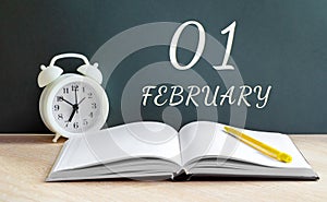 february 01. 01-th day of the month, calendar date.A white alarm clock, an open notebook with blank pages, and a yellow