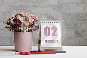 february 02. 02-th day of the month, calendar date.A delicate bouquet of flowers in a pink vase, two pencils and a