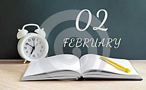 february 02. 02-th day of the month, calendar date.A white alarm clock, an open notebook with blank pages, and a yellow