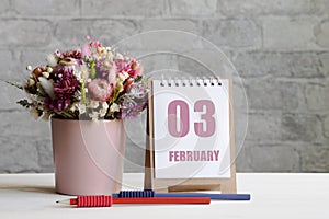 february 03. 03-th day of the month, calendar date.A delicate bouquet of flowers in a pink vase, two pencils and a