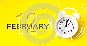 February 12nd. Day 12 of month, Calendar date. White alarm clock with calendar day on yellow background. Minimalistic concept of