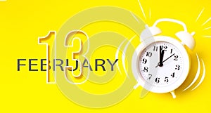 February 13rd. Day 13 of month, Calendar date. White alarm clock with calendar day on yellow background. Minimalistic concept of