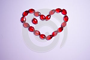 February 14. Heart of beads on a white background in the center. Empty white space. Bright red beads lie in the shape of a heart.