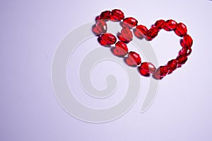 February 14. Heart of beads on a white background in the center. Empty white space. Bright red beads lie in the shape of a heart.