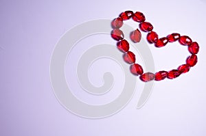 February 14. Heart of beads on a white background in the center. Empty white space. Bright red beads lie in the shape of a heart.