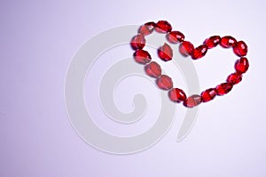 February 14. Heart of beads on a white background in the center. Empty white space. Bright red beads lie in the shape of a heart.