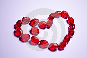 February 14. Heart of beads on a white background in the center. Empty white space. Bright red beads lie in the shape of a heart.