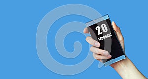february 20. 20th day of the month, calendar date.Woman& x27;s hand holds mobile phone with blank screen on blue isolated