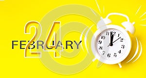 February 24th. Day 24 of month, Calendar date. White alarm clock with calendar day on yellow background. Minimalistic concept of