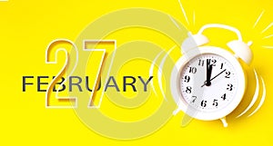 February 27th. Day 27 of month, Calendar date. White alarm clock with calendar day on yellow background. Minimalistic concept of