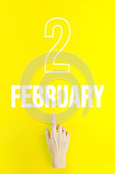 February 2nd. Day 2 of month, Calendar date.Hand finger pointing at a calendar date on yellow background.Winter month, day of the