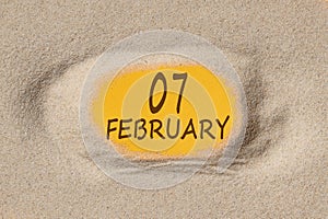 February 7. 7th day of the month, calendar date. Hole in sand. Yellow background is visible through hole