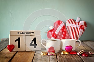 February 14th wooden vintage calendar with colorful heart shape chocolates next to couple cups on wooden table. selective focus