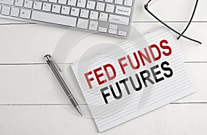 FED FUNDS FUTURES text on notebook with keyboard , pen glasses on white wooden background