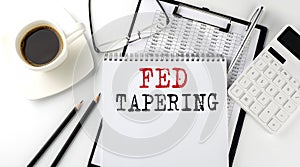 FED TAPERING text on the paper with calculator, notepad, coffee ,pen with graph