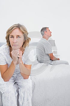 Fed up couple sitting on different sides of bed having a dispute