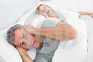 Fed up man blocking his ears from noise of wife snoring