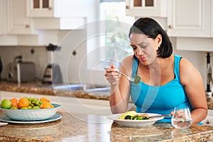 Fed Up Overweight Woman Eating Healthy Meal in Kitchen