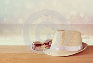 Fedora hat and sunglasses over wooden table and glitter background. relaxation or vacation concept