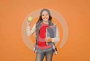 Feed your brain with knowledge. Happy kid hold apple and books orange background. Symbol of knowledge. Back to school