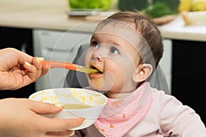 Feeding. Adorable baby child eating with a spoon in a children`s chair