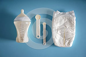 Feeding bottle of baby formula with diaper and powder on color background