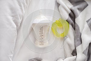 Feeding bottle of baby formula with teether on bed