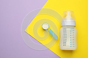 Feeding bottle with infant formula and powder on color background, flat lay. Space for text