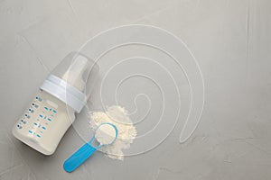 Feeding bottle with infant formula, scoop of powder and space for text on grey table, flat lay. Baby milk