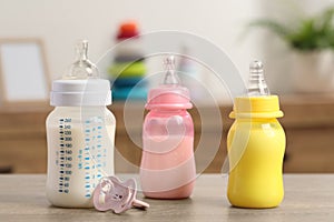 Feeding bottles with baby formula and pacifier on wooden table indoors