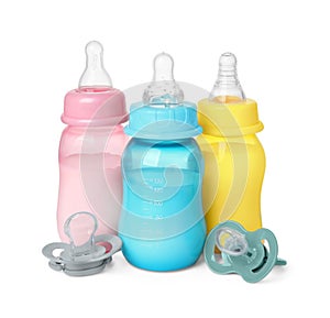 Feeding bottles with milk and pacifiers on white background