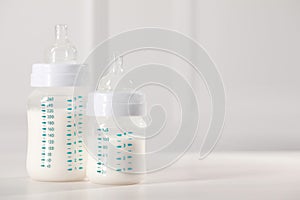 Feeding bottles with milk on white wooden table. Space for text