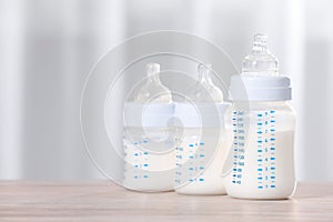 Feeding bottles with milk on wooden table indoors. Space for text