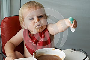 Feeding chair, eating and baby with spoon in a house for food, nutrition and fun while playing. Food, messy eater and