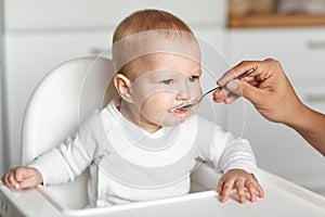 Feeding of cute baby with a spoon in the kitchen